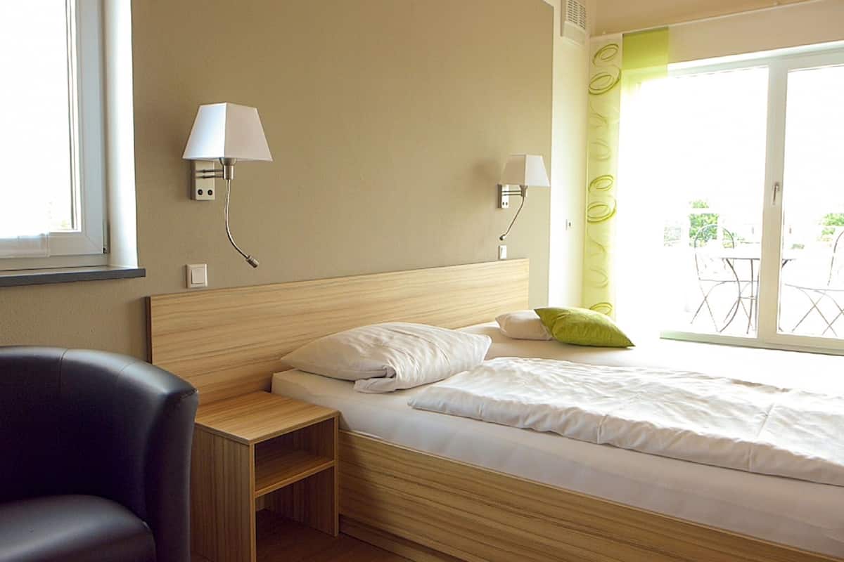 A hotel room with a bed, a chair, a nightstand, and two wall-mounted lamps.