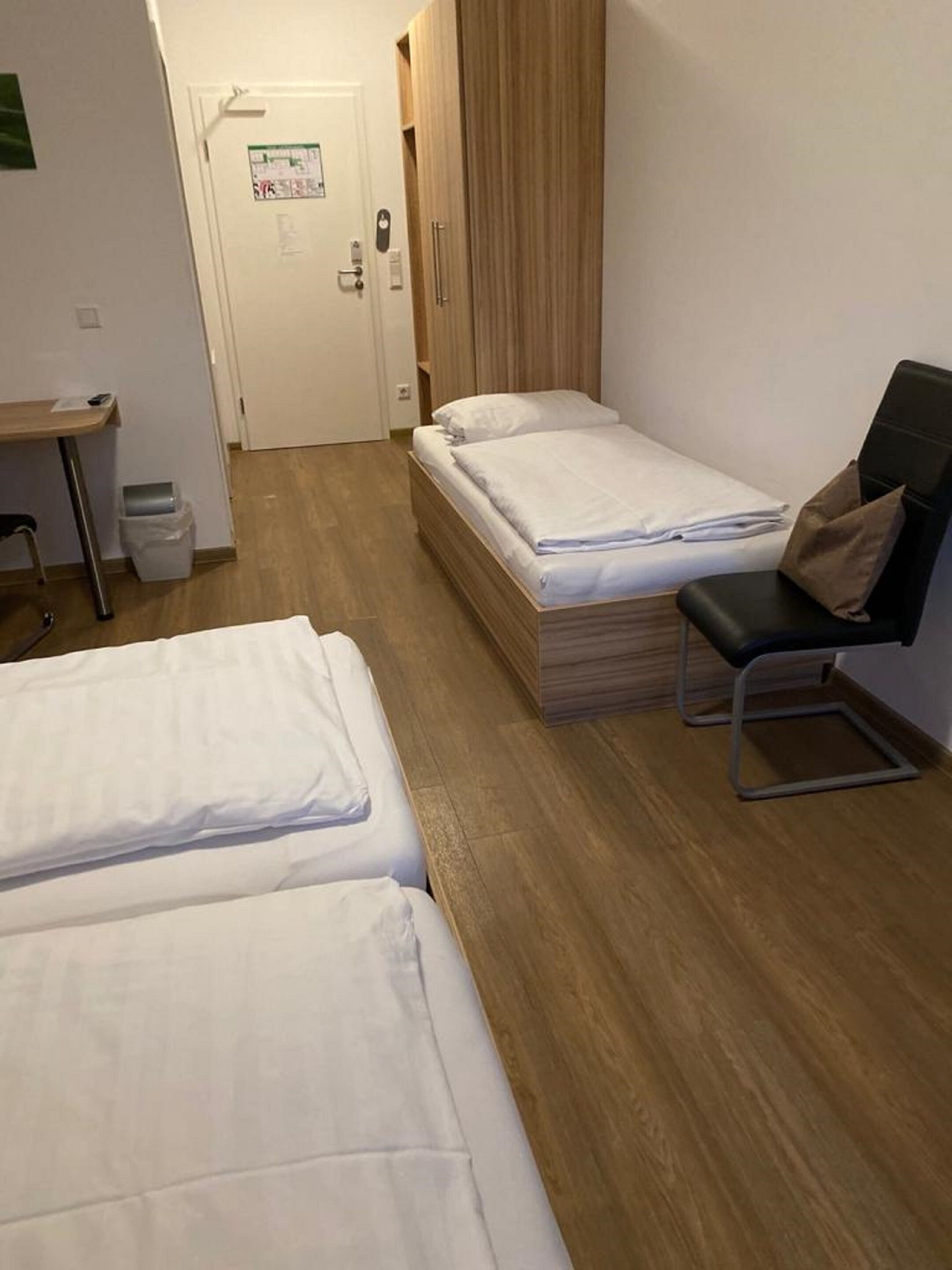 A hotel room with two single beds, a desk, a chair, and a wooden wardrobe.