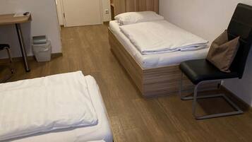 A hotel room with two single beds, a desk, a chair, and a wooden wardrobe.