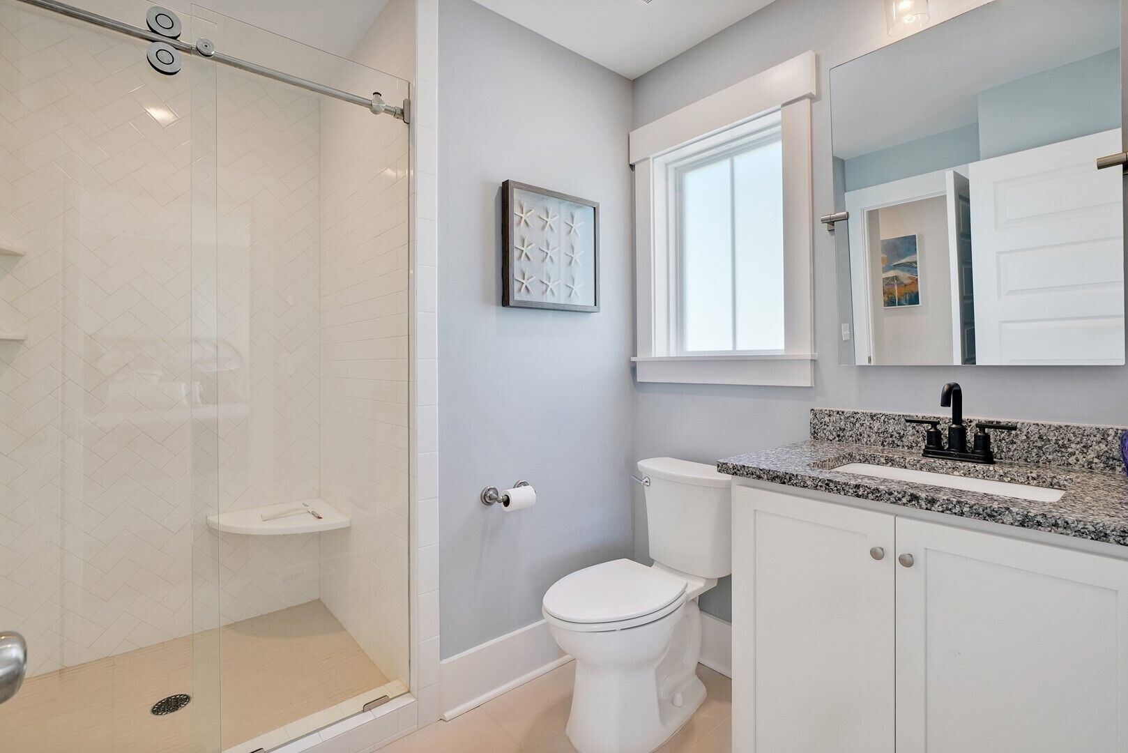 Une salle de bain dotée d’une douche à parois de verre, de toilettes, d’un lavabo avec un plan de travail en granit et d’un miroir au-dessus du lavabo.
