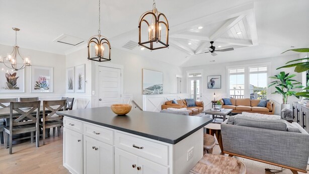 Una cocina amplia con una isla central, un comedor con mesa y sillas de madera, una sala de estar con sofá y una mesa de centro, y un ventilador de techo.