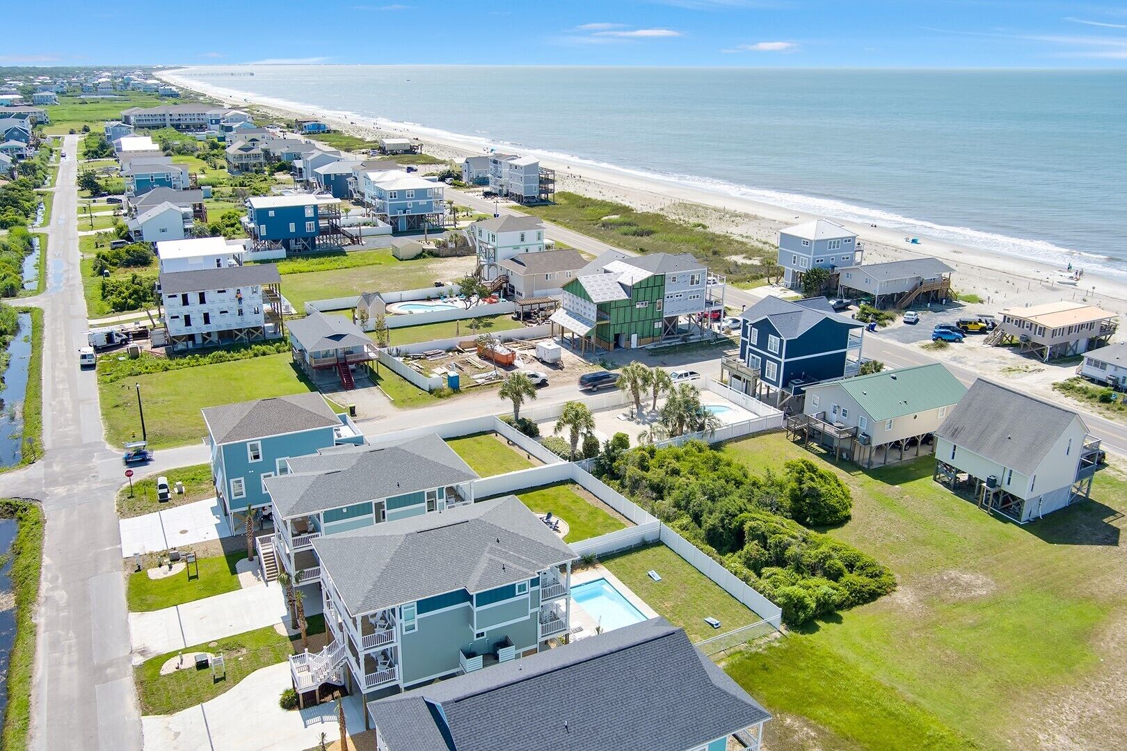 Vue aérienne d’une zone résidentielle côtière, avec des maisons, une plage et un ciel dégagé.