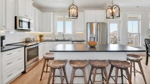Una cocina moderna con armarios blancos, electrodomésticos de acero inoxidable y taburetes de madera.