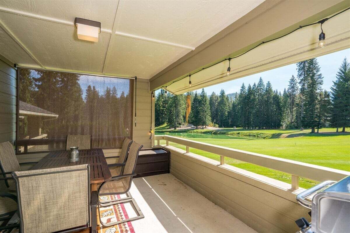 A covered porch with a table and chairs, a view of a golf course, and a wooden deck railing.