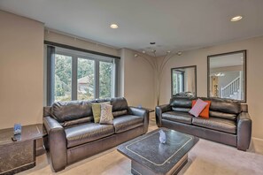 A spacious living room with two leather sofas, a coffee table, and large windows offering a view of the outdoors.