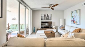 A modern living room with a large TV, comfortable seating, and a ceiling fan. - Jupiter Bay Condo w/ Pool < Half Mile to Beach! (Jupiter)