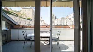 A balcony with a glass door, two chairs, a small round table, and a view of buildings in the background. - HbHall - Duomo Suite 7 Apartment (Milan)