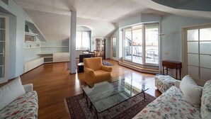 A spacious living room with a high ceiling, wooden flooring, a glass coffee table, and a sofa with floral upholstery. - HbHall - Duomo Suite 7 Apartment (Milan)