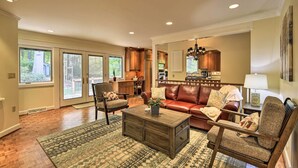 A spacious living room with a brown leather sofa, two armchairs, a coffee table, and a rug. There is a dining area with wooden cabinets and a chandelier. - Easy Hiking & Sightseeing! Kingsport Home w/ Deck (Kingsport)
