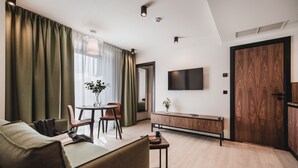 A modern living room with a sofa, a dining table with chairs, a TV mounted on the wall, and a wooden cabinet. - Apartamenty Sowa Bydgoszcz (Bydgoszcz)