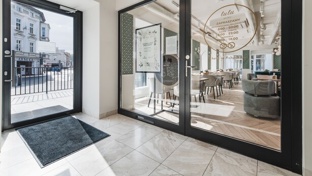 A modern hotel lobby with a large glass door leading to a seating area and a view of the street. - Apartamenty Sowa Bydgoszcz (Bydgoszcz)