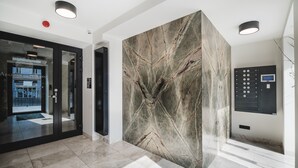 A modern lobby with a marble wall, glass doors, and a digital elevator control panel. - Apartamenty Sowa Bydgoszcz (Bydgoszcz)