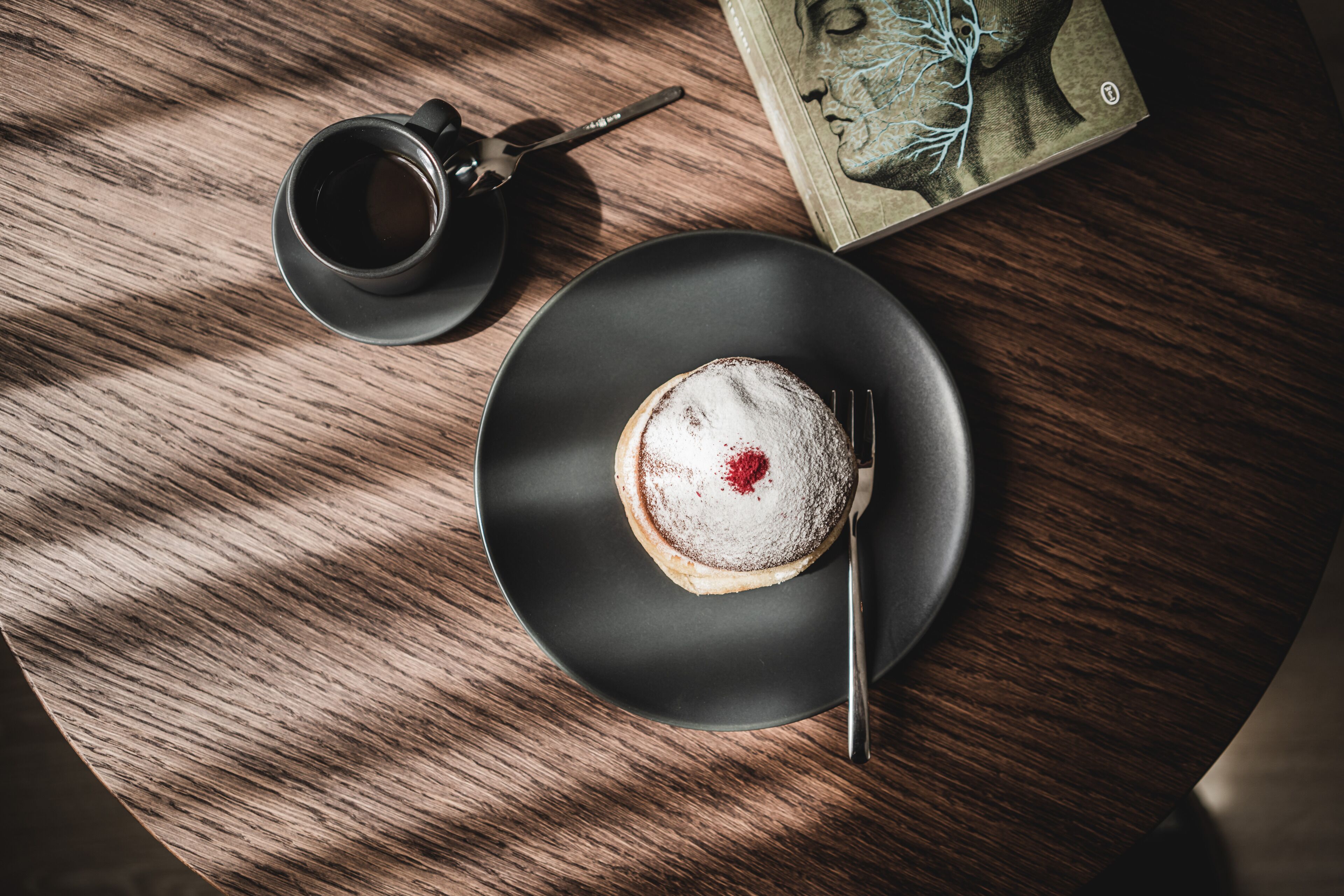 Un tavolo rotondo con un piatto di cibo, una tazza di caffè e un libro.