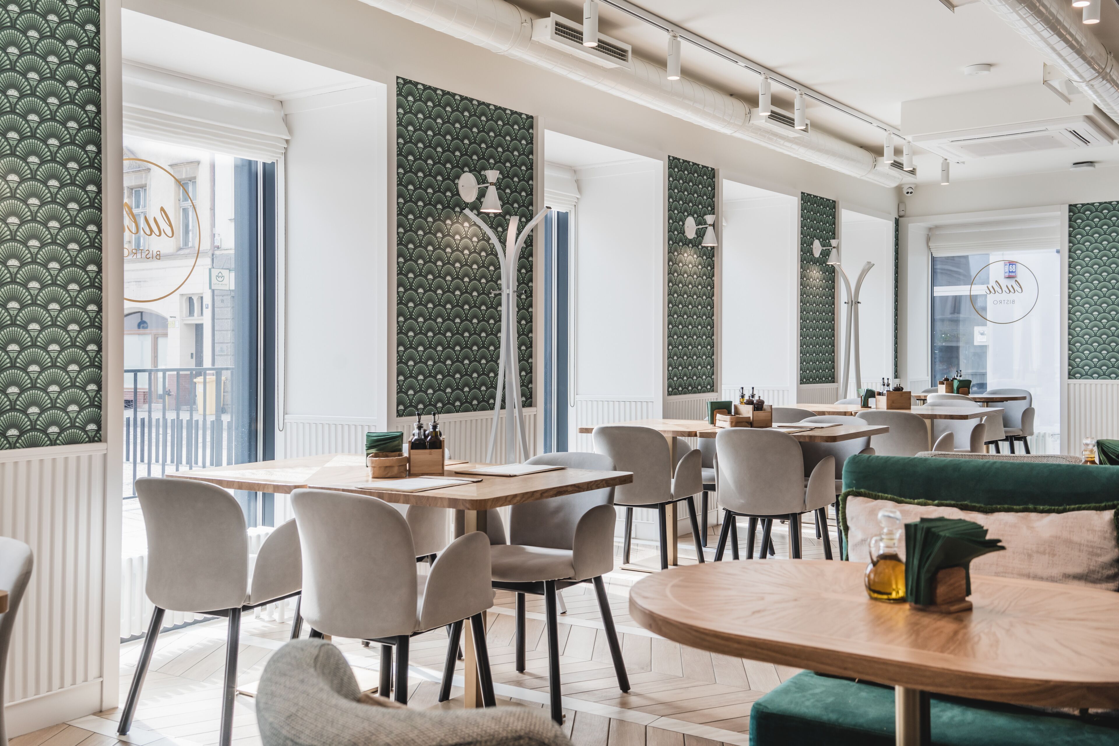 A modern dining area with high ceilings, large windows, and green patterned walls.