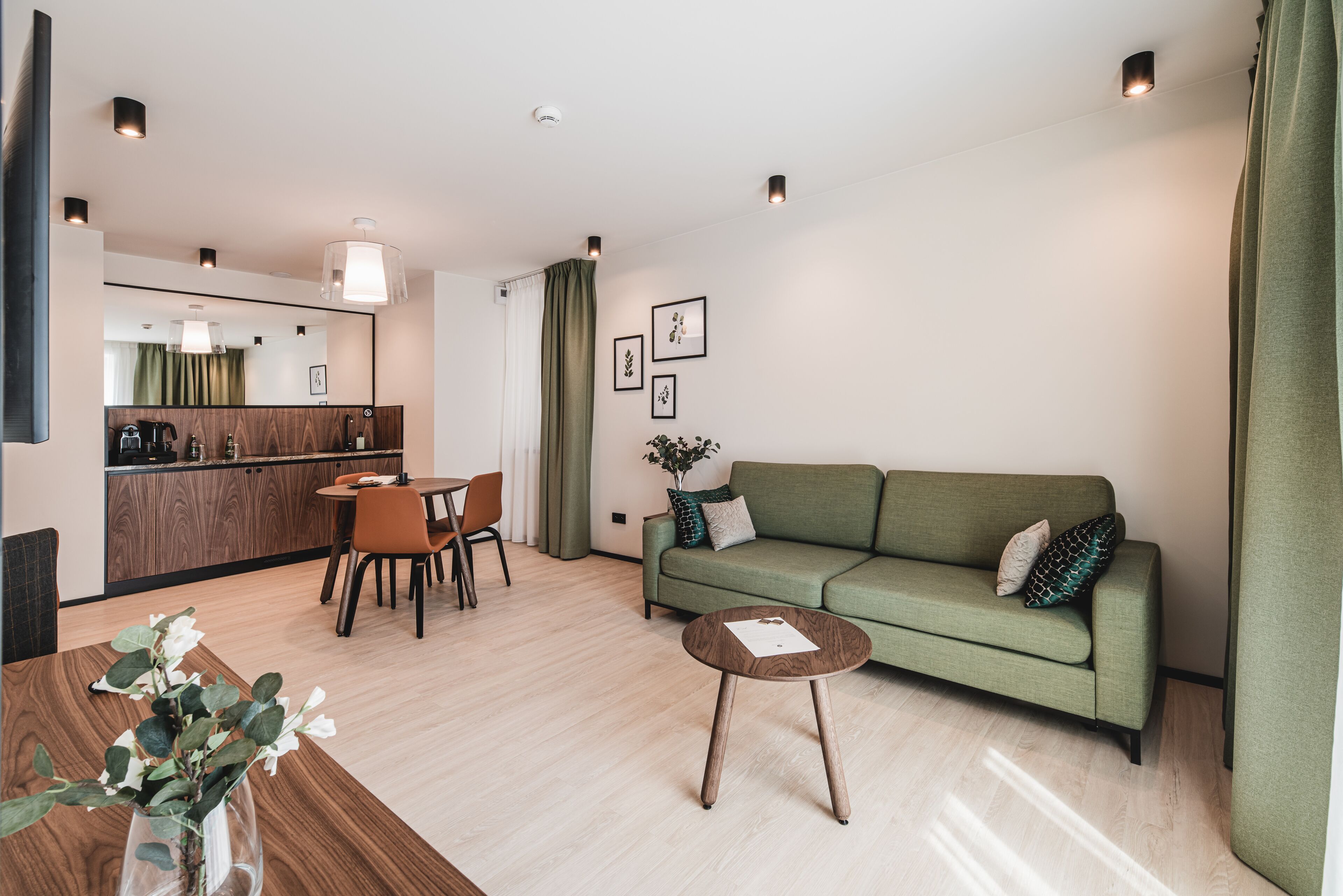 A modern living room with a green sofa, a wooden coffee table, and a dining area with a table and chairs.