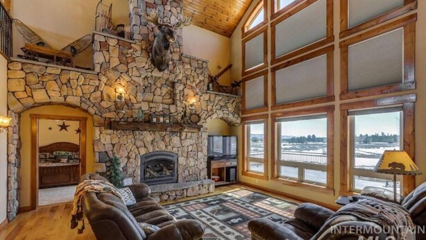 A spacious living room with a stone fireplace, leather sofas, and large windows offering a view of a snowy landscape.