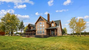 A large, two-story wooden house with a prominent chimney, a covered porch, and a spacious front yard.