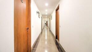 A hotel corridor with wooden doors, white walls, and a polished floor. - Hotel Airport View (New Delhi)