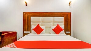 A hotel room with a wooden headboard, white bedding, and two red pillows. - Hotel Airport View (New Delhi)