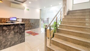 A hotel reception area with a marble counter, a computer, a fire exit sign, and a staircase leading to another floor. - Hotel Airport View (New Delhi)