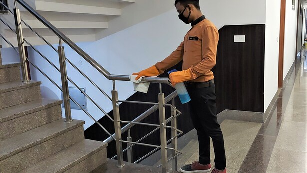 A person cleaning a staircase with a cloth and spray bottle. - Hotel Airport View (New Delhi)