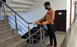 A person cleaning a staircase with a cloth and spray bottle. - Hotel Airport View (New Delhi)