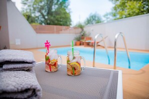 Dues gots de vidre amb una beguda, una pila de tovalloles i un ambient de piscina.