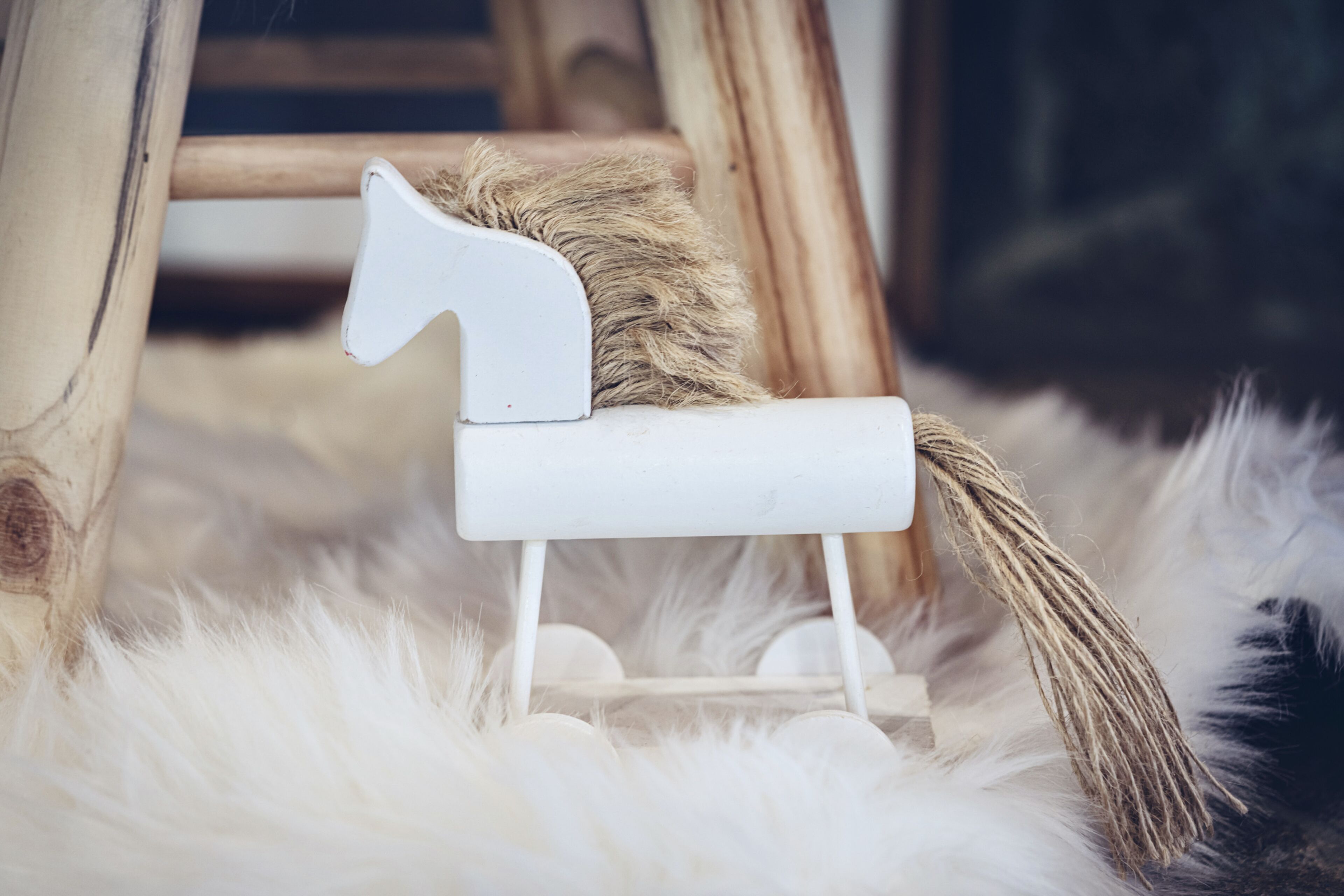 Un cheval à bascule blanc, avec une crinière et une queue brunes, posé sur une surface blanche et moelleuse.