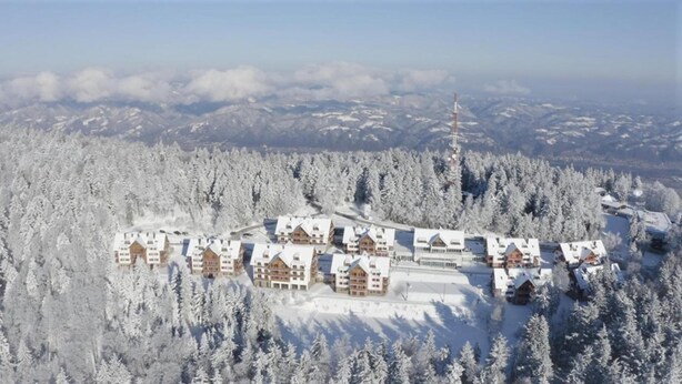 A snow-covered lodge with multiple buildings, surrounded by dense forest and mountains. - Pohorje Village Wellbeing Resort – Forest Apartments Videc (Maribor)