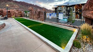 A pool area with a green artificial turf, a building with a modern design, and a mountainous backdrop. - Beautiful Brand NEW Luxury Condo @ Sage Creek (Moab)