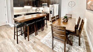 A modern kitchen with dark cabinets, stainless steel appliances, and a wooden dining table with chairs. - Beautiful Brand NEW Luxury Condo @ Sage Creek (Moab)
