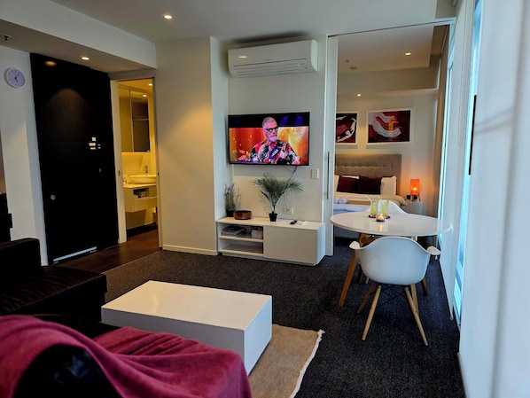 Una habitación de hotel moderna con televisión de pantalla plana, zona de comedor, sofá y dormitorio independiente.
