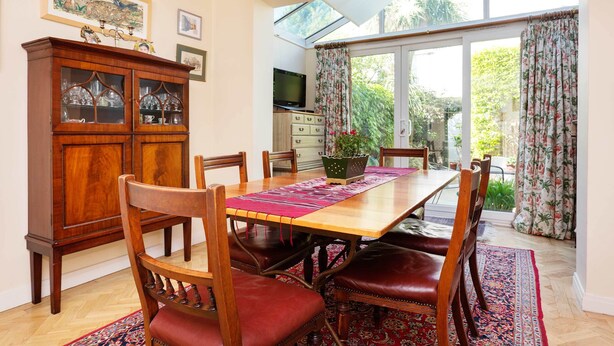 A dining area with a wooden table, red cushioned chairs, a glass cabinet, and a large window with curtains.