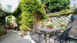 A patio with a table and chairs, surrounded by potted plants and a brick wall.