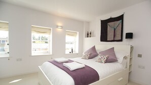 A bedroom with a bed, two windows, a wall-mounted light, and a black object on the wall. - Modern Edwardian, by Veeve (London)