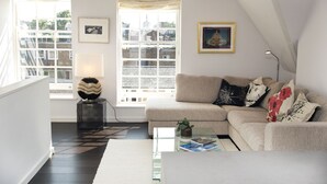 A modern living room with a sofa, a coffee table, and a lamp. There are two windows with curtains, and a picture frame on the wall. - Modern Edwardian, by Veeve (London)