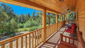 Eine überdachte Veranda mit Holzgeländern, eine Sitzecke mit roten Kissen und Blick auf eine bewaldete Landschaft.