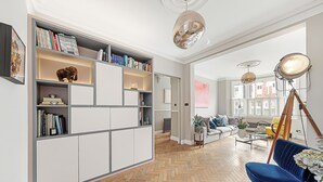 A modern living room with a herringbone wooden floor, white built-in shelving with books, a blue sofa, and a floor lamp. - Clapham Fairytale, by Veeve (London)