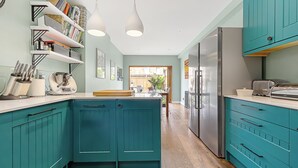 A kitchen with teal cabinetry, a central island, and a view to the outdoors. - Clapham Fairytale, by Veeve (London)