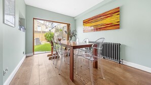 A dining area with a wooden table and clear chairs, a radiator, and a large abstract painting on the wall. - Clapham Fairytale, by Veeve (London)