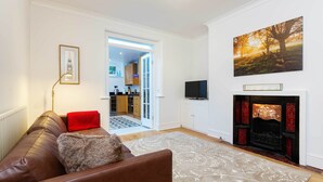Ein Wohnzimmer mit Kamin, einer Couch, einer roten Decke und einem gerahmten Bild an der Wand.