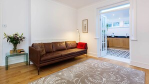 Ein modernes Wohnzimmer mit einem braunen Ledersofa, einem Glastisch und einem gemusterten Teppich.
