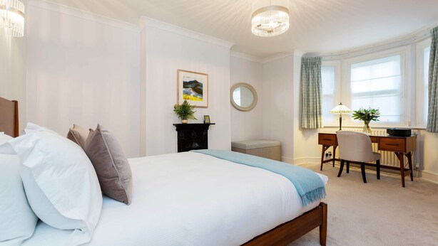 Ein Schlafzimmer mit Bett, Schreibtisch, Stuhl, Heizkörper und einem Fenster mit Vorhängen.