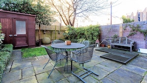 Eine Terrasse mit einem runden Tisch und Stühlen, eine kleine Gartenhütte und ein Holzzaun.