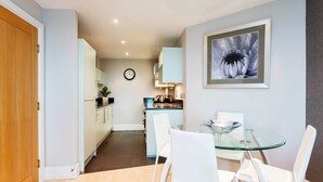 A modern kitchen with white cabinets, a glass dining table, and white chairs.