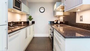 A modern kitchen with white cabinets, granite countertops, a microwave, and a clock on the wall.