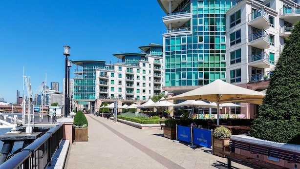 A waterfront hotel with multiple balconies, a covered outdoor seating area, and a marina in the background.