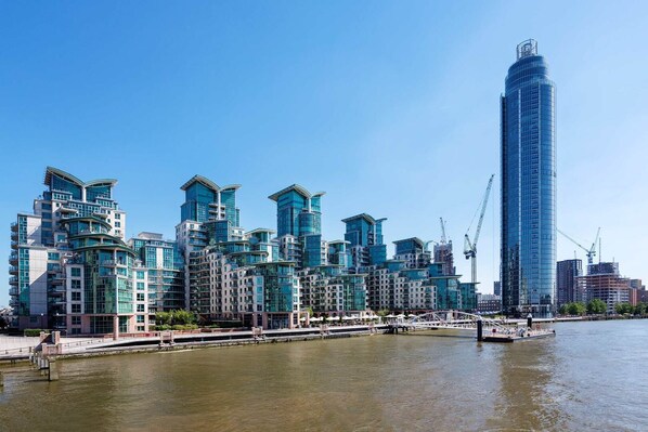 A modern high-rise building with a glass facade, situated next to a body of water with a bridge in the foreground. - River Views from Vauxhall, by Veeve (London)