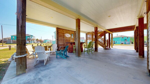 A covered outdoor area with wooden pillars, a concrete floor, and several chairs. - Adicora Beach House: 3 BR, 2 BA House in Port Bolivar, Sleeps 14 (Bolivar Peninsula)