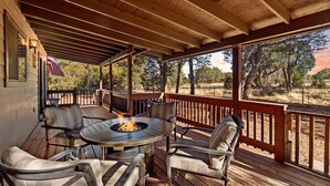 A covered outdoor patio with a fire pit table and chairs, overlooking a natural landscape. - High Country Escape | Forest Border • Fenced Yard (Heber)